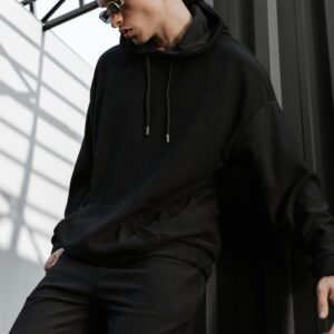 Home Stylish young adult in black hoodie and sunglasses posing against industrial backdrop.